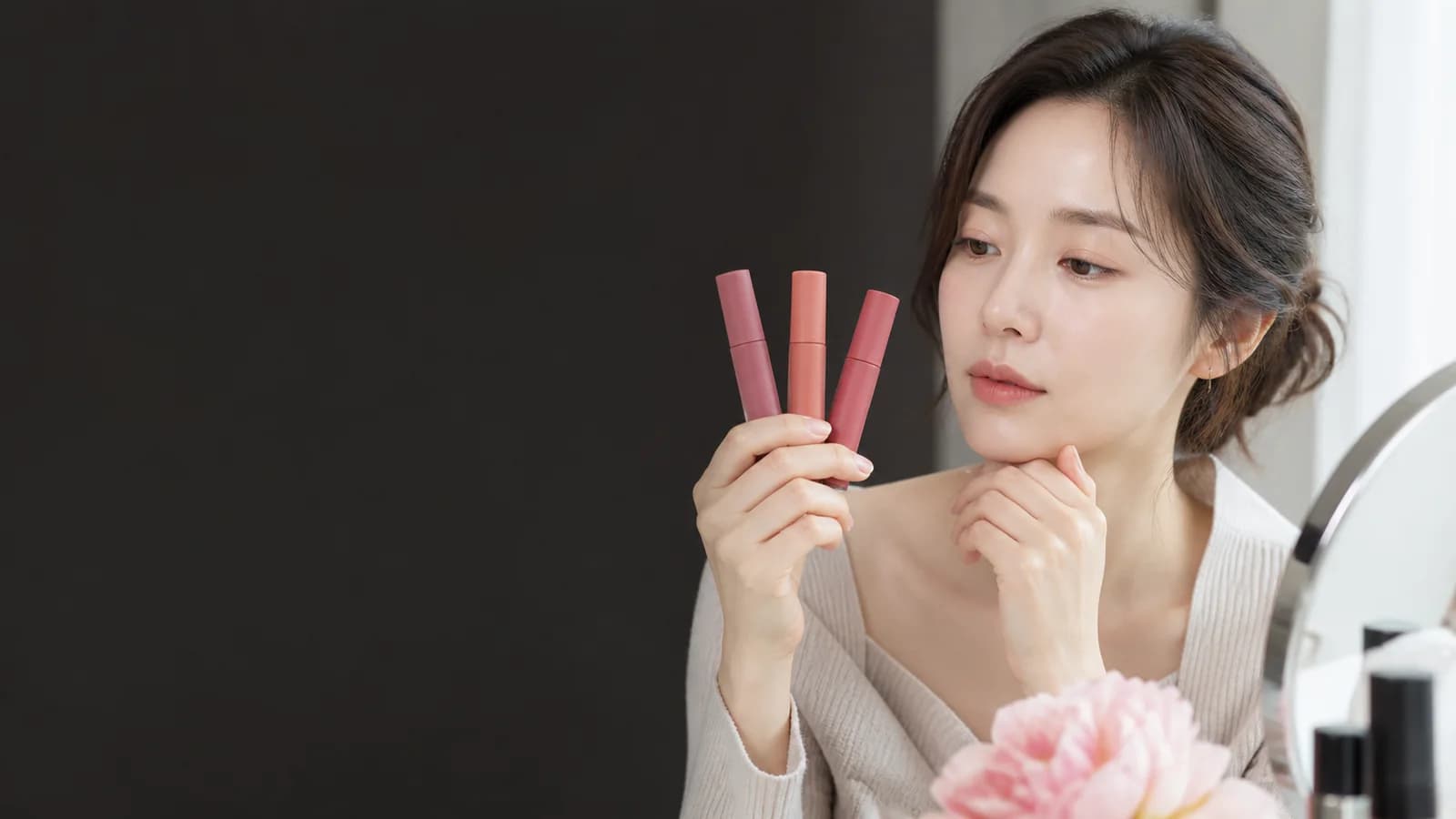 세 가지 립 제품과 색상 카드를 창가에서 비교하는 성인 한국인 여성