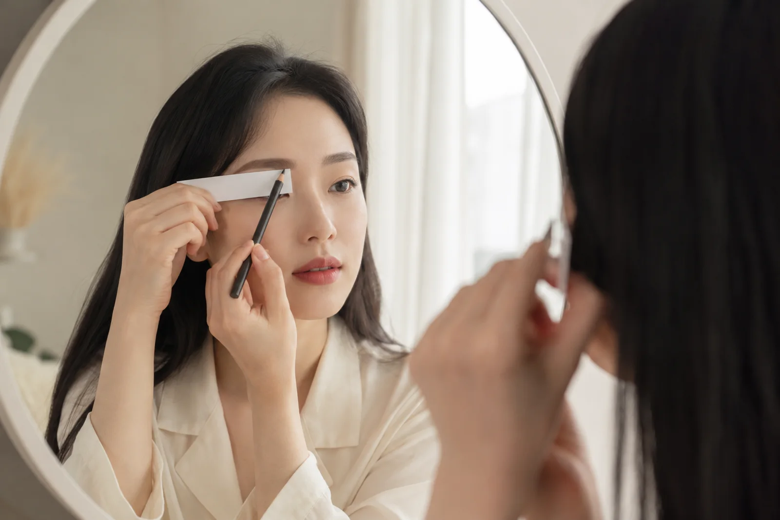 거울과 눈썹 연필 옆 무문자 카드에 평소 손질 범위를 표시하는 한국 성인 여성