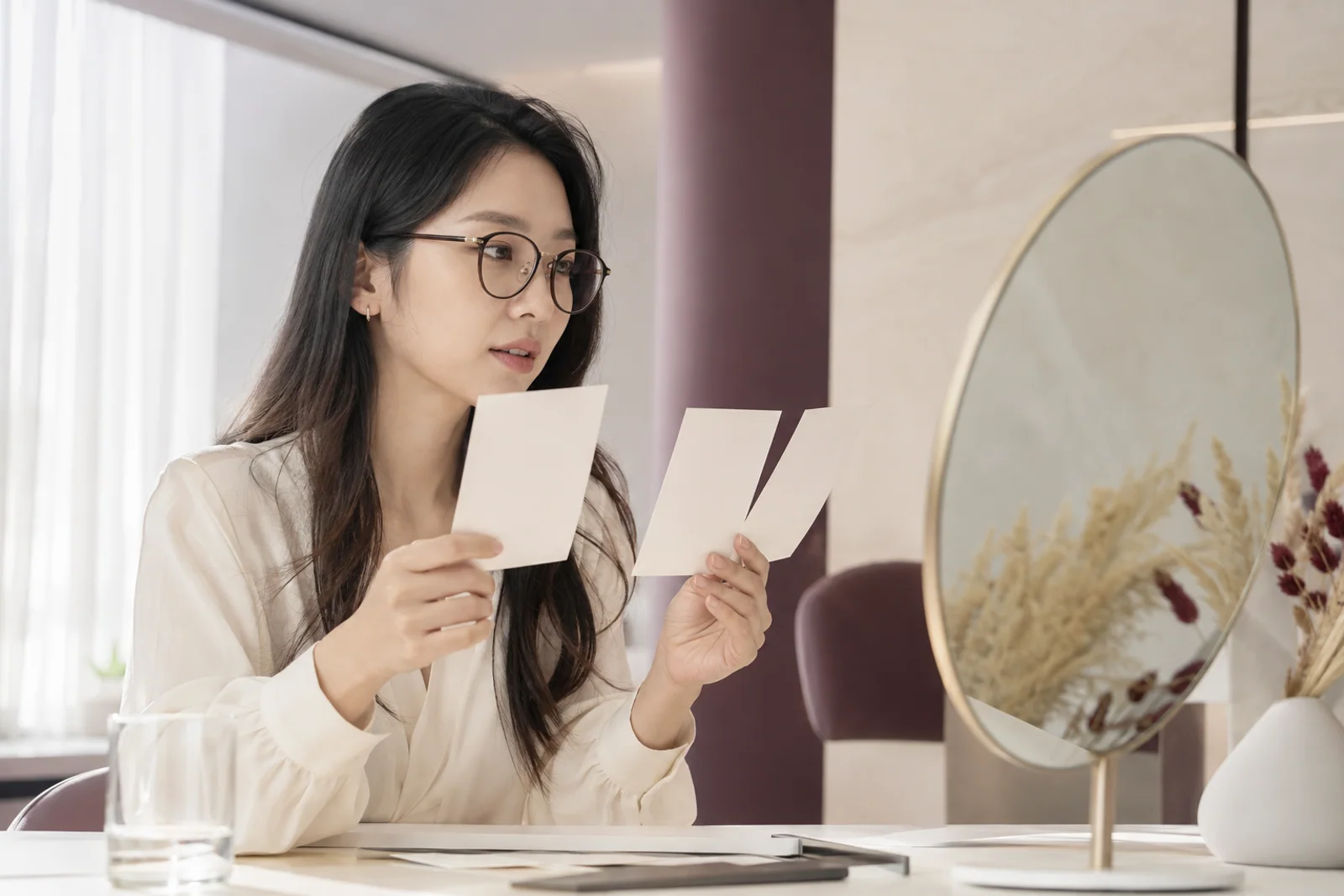 안경과 아이라인 메이크업 참고 카드를 거울 옆에서 비교하는 한국 성인 여성