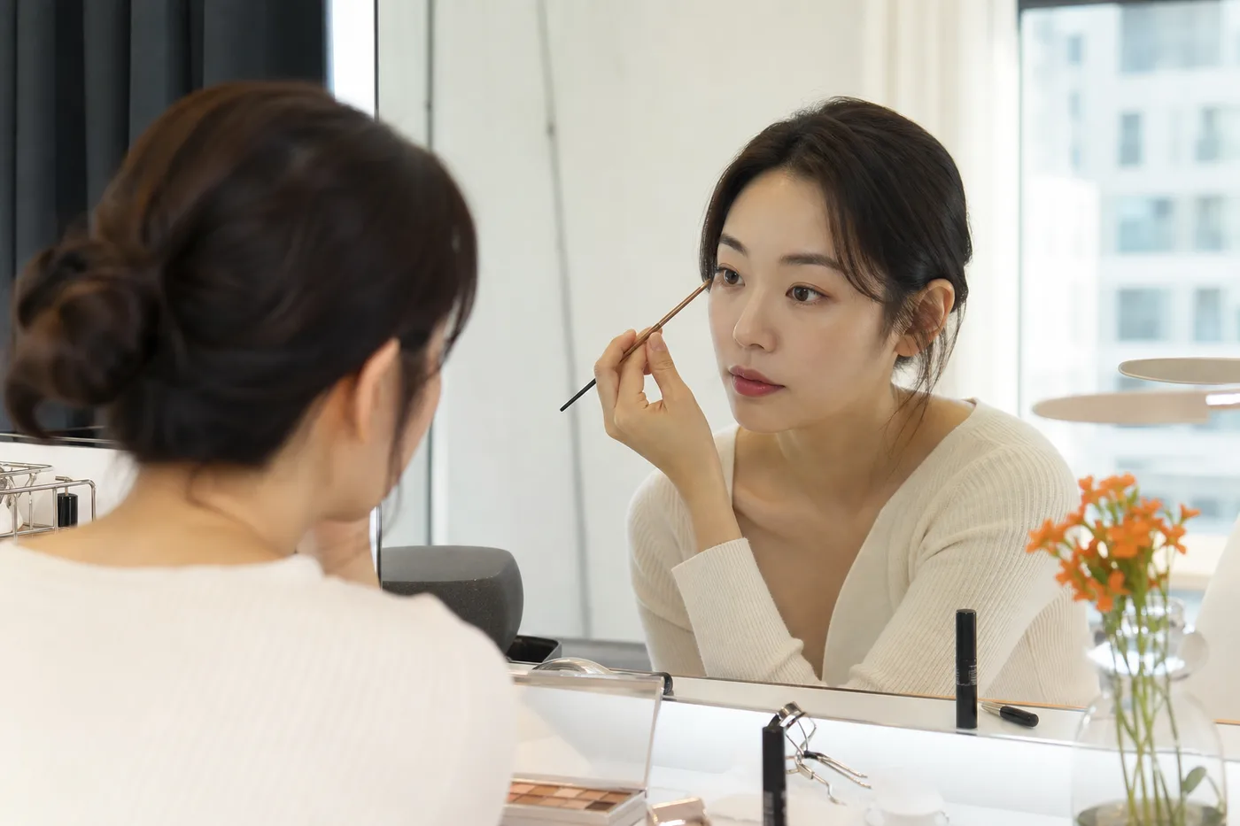 거울 앞에서 가벼운 눈화장 손동작을 확인하는 한국 성인 여성