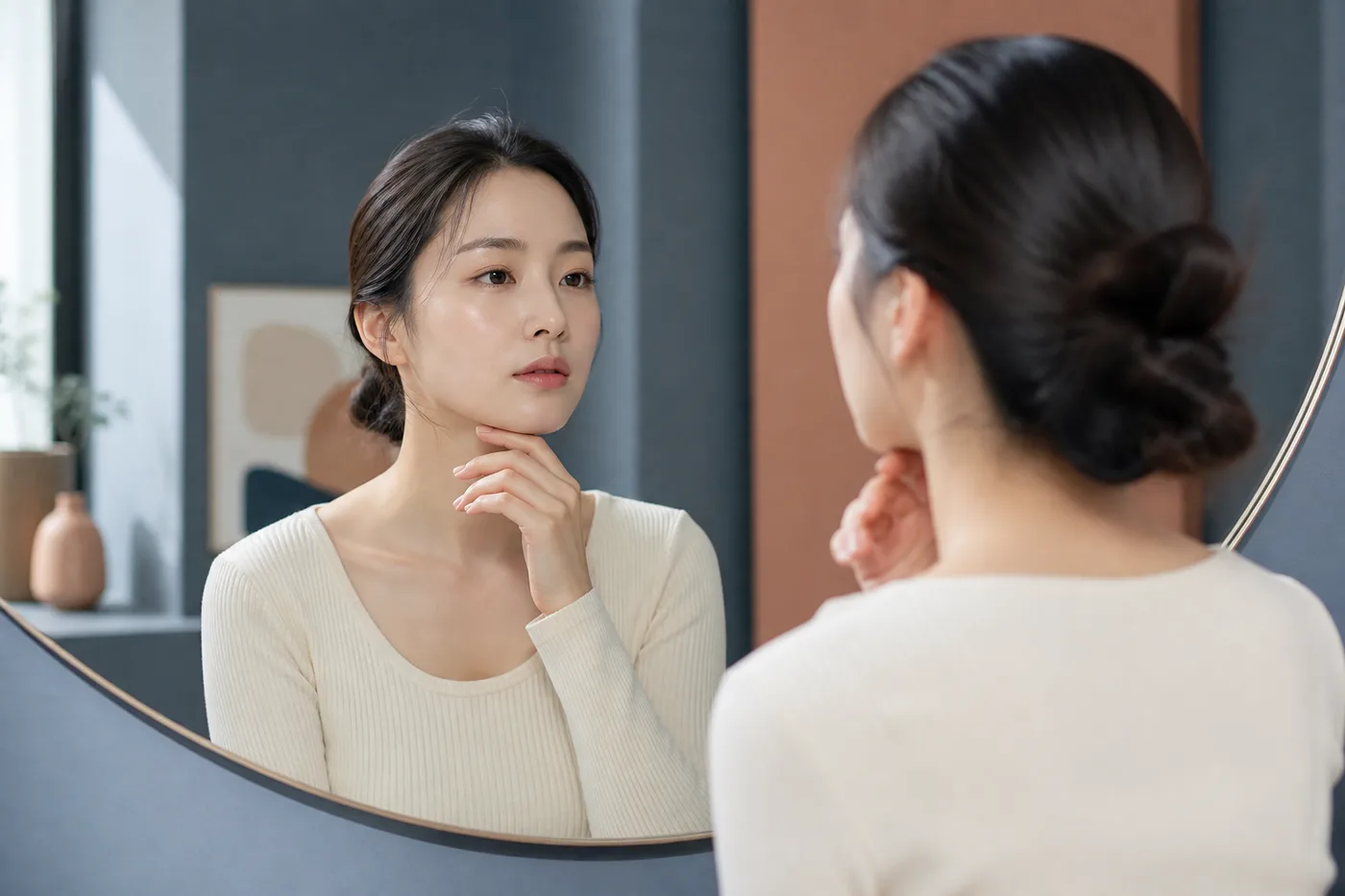 머리를 묶고 헤어라인과 눈썹 윤곽을 거울로 살펴보는 한국 여성